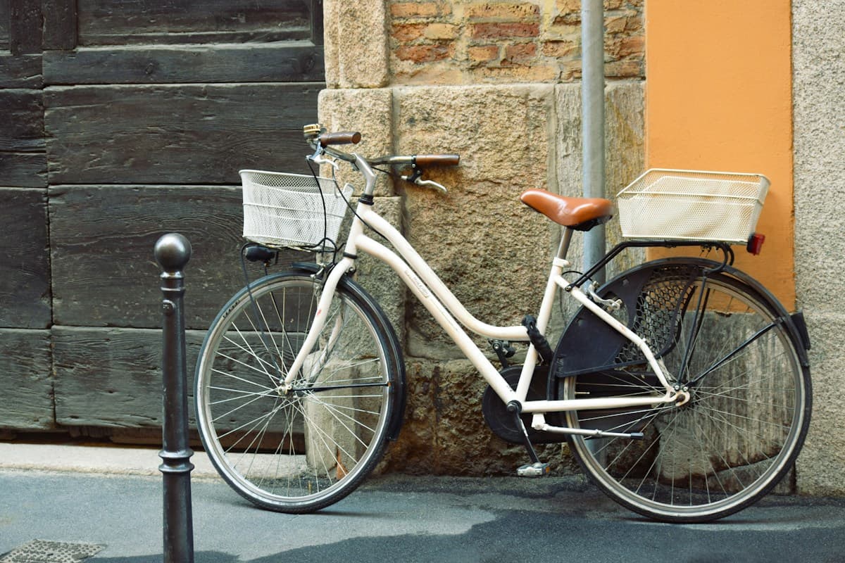A white city bicycle with baskets against a weathered wall